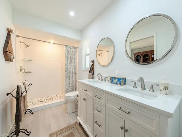 Full bath featuring toilet, a sink, double vanity, and tiled shower