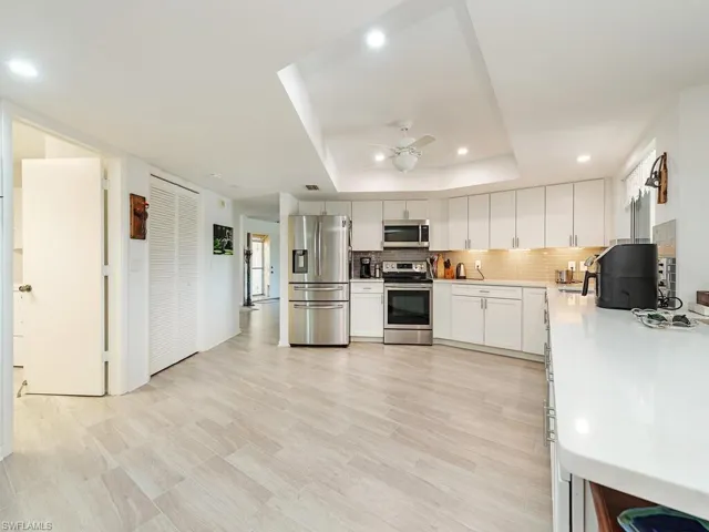 Kitchen with light countertops, backsplash, a raised ceiling, appliances with stainless steel finishes, and ceiling fan