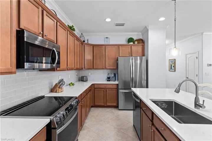 Kitchen with appliances with stainless steel finishes, brown cabinetry, ornamental molding, tasteful backsplash, and decorative light fixtures