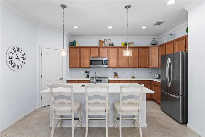 Kitchen featuring appliances with stainless steel finishes, brown cabinetry, crown molding, tasteful backsplash, and a kitchen breakfast bar