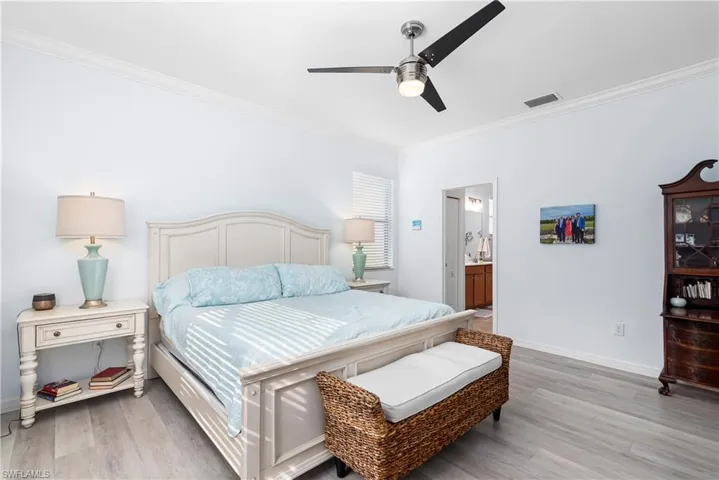 Bedroom featuring ornamental molding, light wood-style flooring, ceiling fan, and ensuite bath