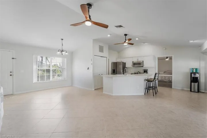 Kitchen featuring pendant lighting, lofted ceiling, white cabinets, appliances with stainless steel finishes, and a breakfast bar area