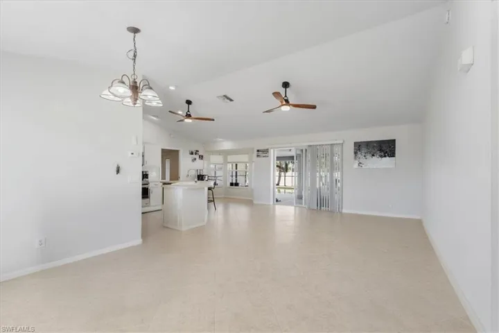 Unfurnished living room with ceiling fan with notable chandelier, high vaulted ceiling