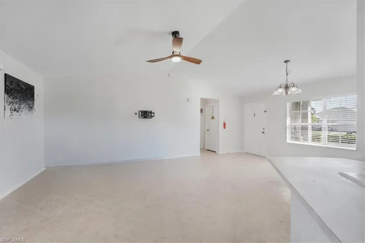 Unfurnished living room featuring ceiling fan with notable chandelier and vaulted ceiling