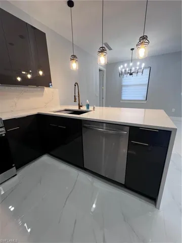 Kitchen featuring dark cabinetry, light stone counters, stainless steel appliances, and hanging light fixtures