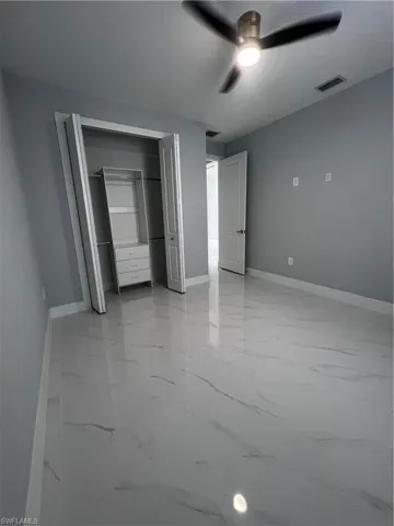 Unfurnished bedroom featuring light marble finish floors, a ceiling fan, and a closet