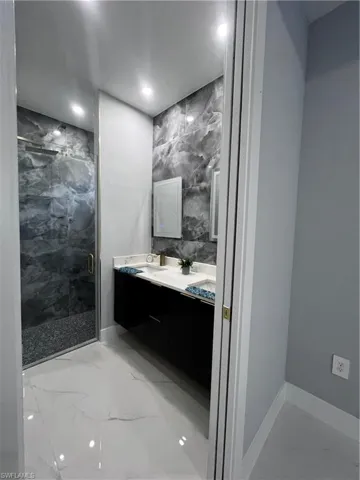 Bathroom with light marble finish floors, double vanity, a marble finish shower, recessed lighting, and tile walls