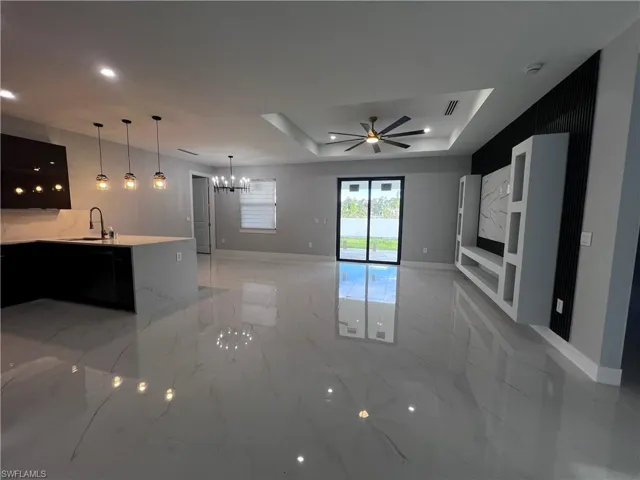 Kitchen with suspended lighting, light stone countertops, dark cabinetry, ceiling fan, and a tray ceiling