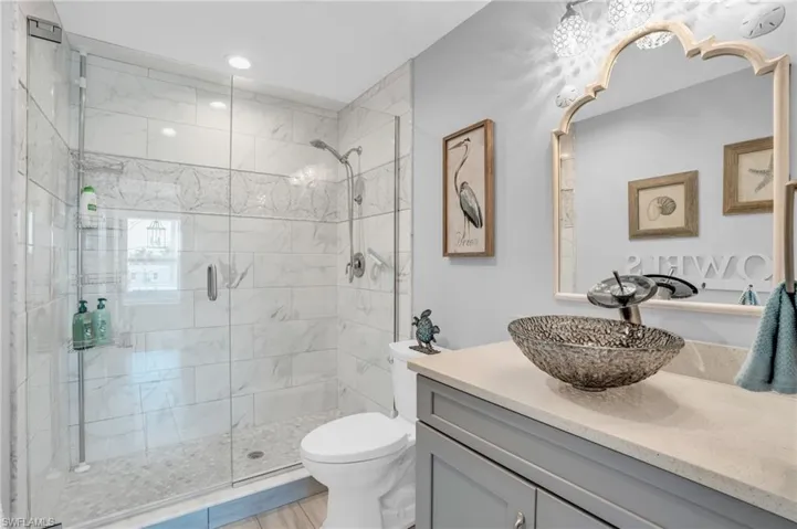 Bathroom featuring vanity with extensive cabinet space, toilet, and a shower with door