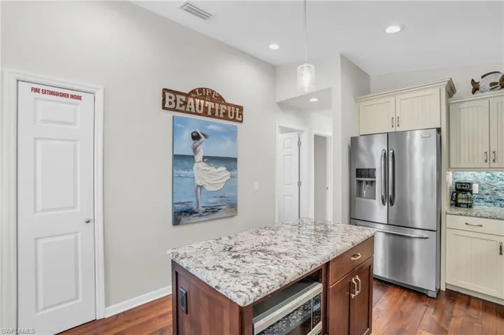 Kitchen featuring dark hardwood / wood-style floors, light stone countertops, stainless steel appliances, hanging light fixtures, and a center island