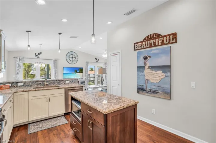 Kitchen featuring light stone countertops, vaulted ceiling, pendant lighting, and dark wood-type flooring