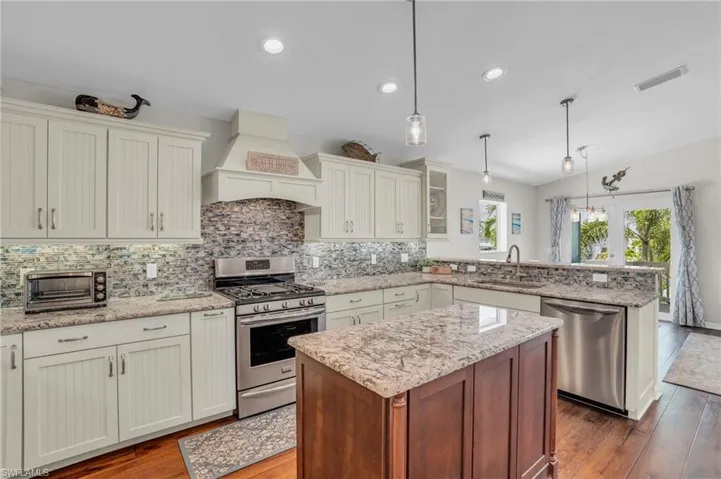 Kitchen featuring stainless steel appliances, hanging light fixtures, sink, and custom range hood