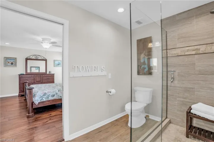 Bathroom featuring a shower with door, ceiling fan, toilet, and hardwood / wood-style floors