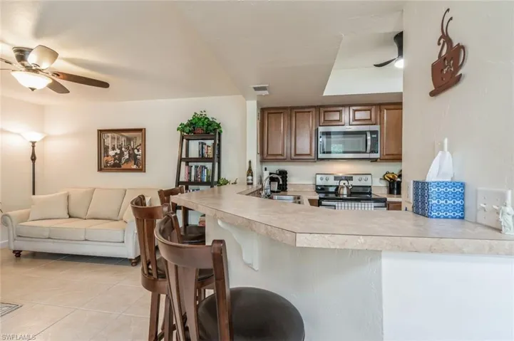 Kitchen with stainless steel appliances, ceiling fan, a kitchen bar, sink, and light tile floors