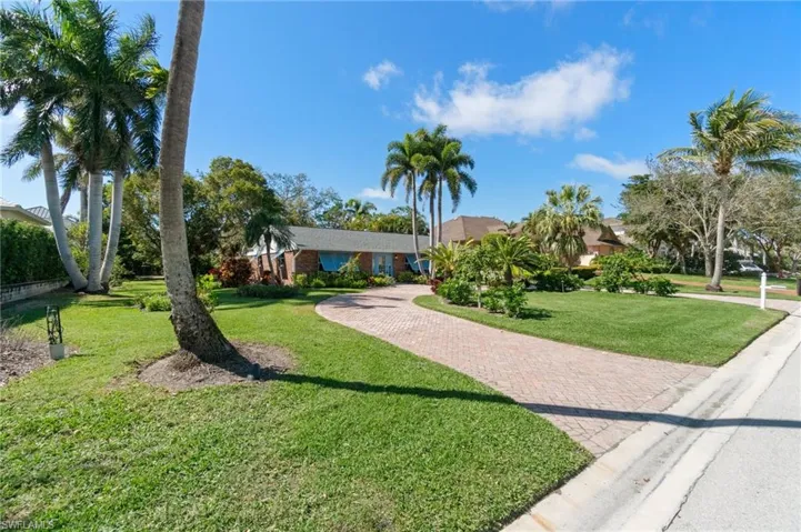 View of front of existing Florida rancher with paver, circular driveway and mature, tropical landscaping.