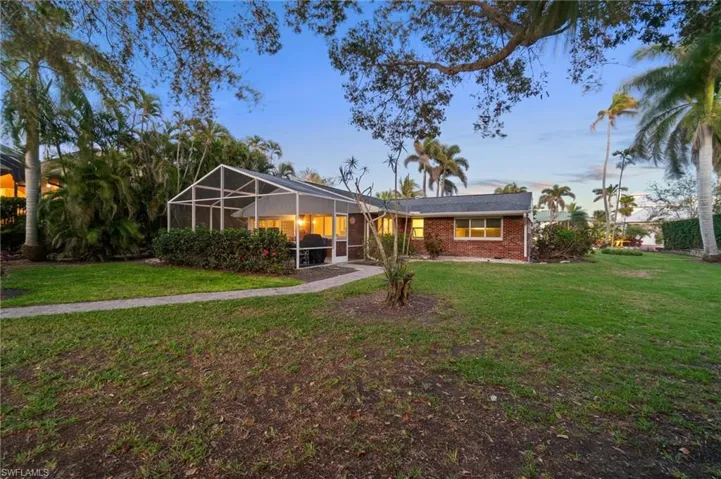 Back of property with brick siding, a lawn, and a lanai