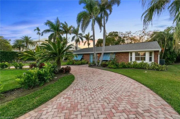 View of front of home featuring brick siding, decorative driveway, and a Expensive tropical yard with mature landscaping.