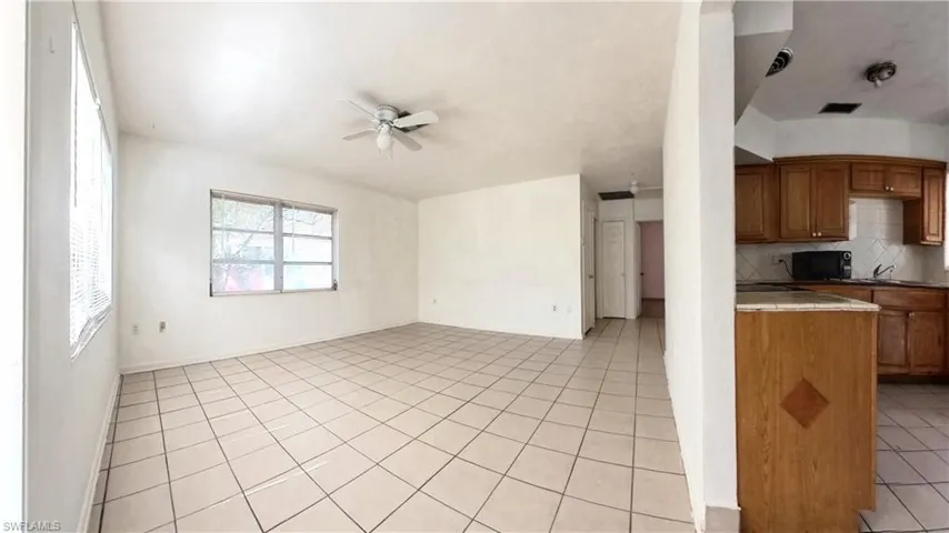 Kitchen featuring light tile patterned flooring, wood finish cabinets, ceiling fan, black microwave, and open floor plan