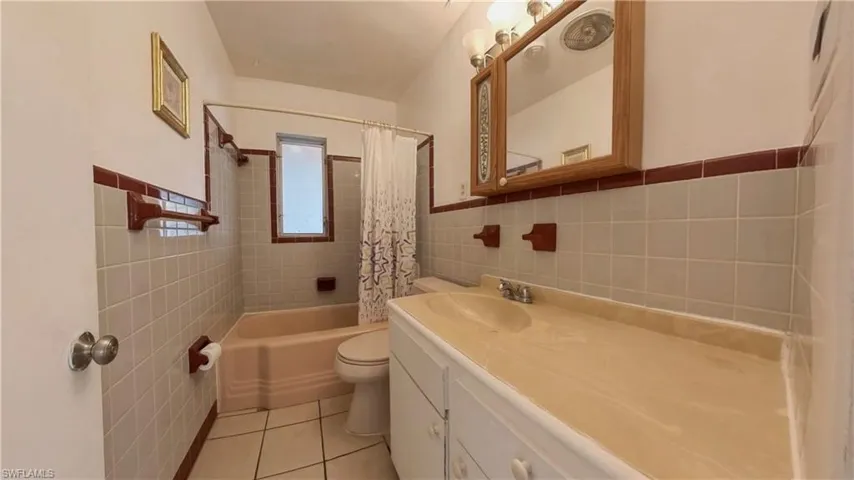 Bathroom featuring tile walls, vanity, shower / tub combo with curtain, and light tile patterned flooring