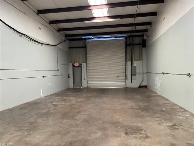 Spacious interior with a roll-up door, exposed structural beams, concrete flooring, and an exit door