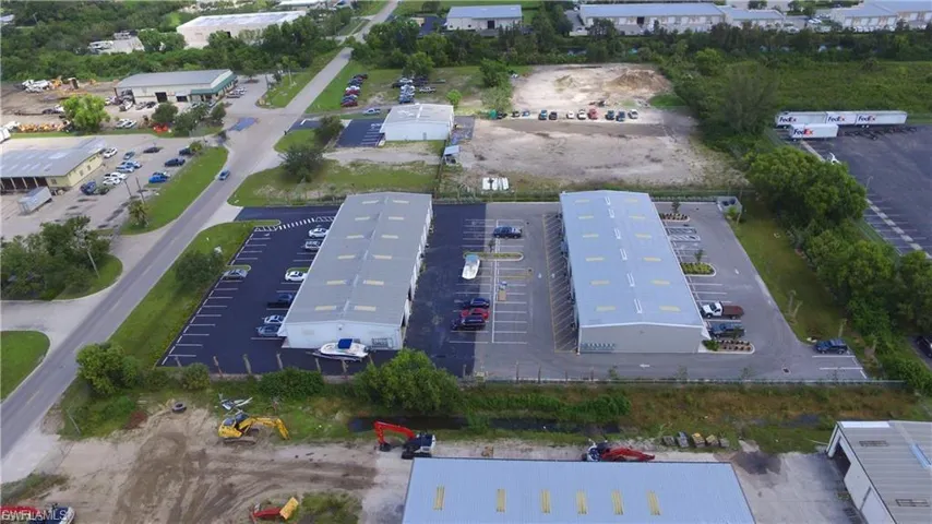 Two industrial-style buildings featuring light-colored roofs and numerous parking spaces