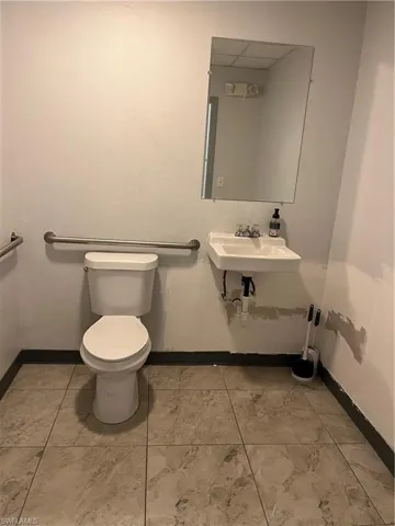 White pedestal sink with a wall-mounted mirror, ceramic toilet, and grab bars