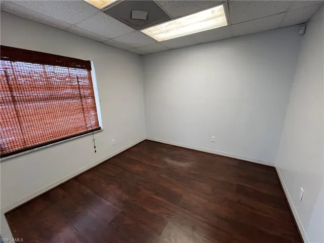 Room featuring dark wood-finish flooring, light-toned walls, and a large window with a woven wood shade