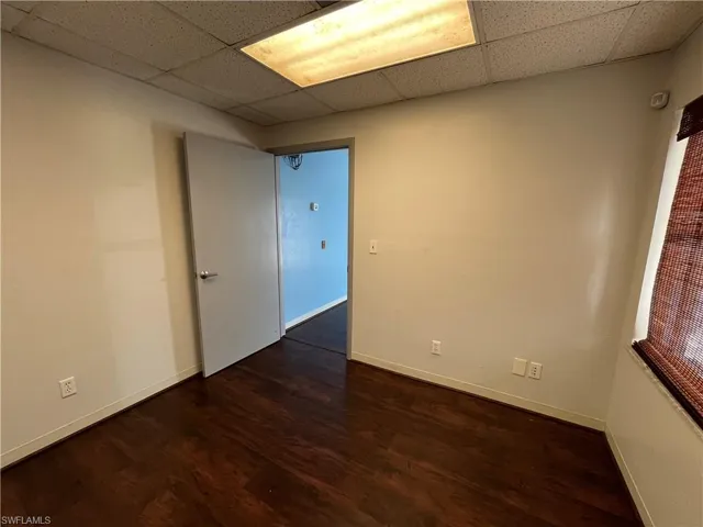 Office space featuring wood-finish flooring, drop ceiling with fluorescent lighting, light-toned walls, and a window with blinds