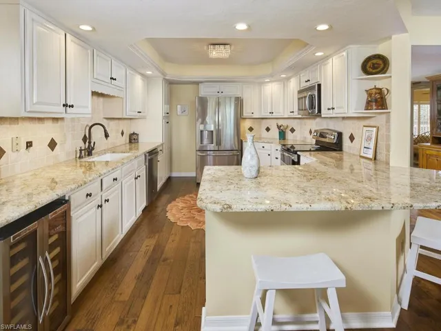 Kitchen featuring large sink, a breakfast bar, appliances with stainless steel finishes, white cabinets, and a tray ceiling