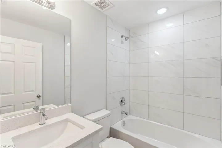 Full bathroom with tiled shower / bath combo, toilet, and vanity with quartz countertop