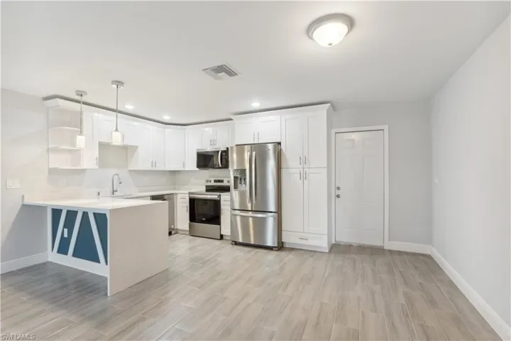 Kitchen featuring kitchen peninsula, white cabinetry, hanging light fixtures, and appliances with stainless steel finishes