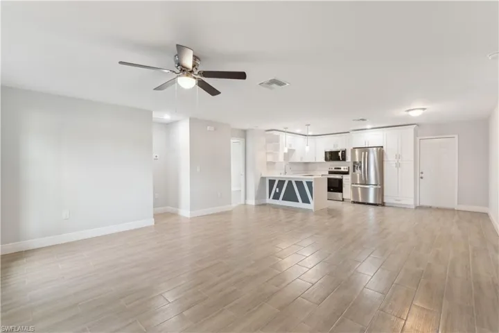 Unfurnished living room with ceiling fan, dining area next to kitchen and light hardwood/wood-style floors