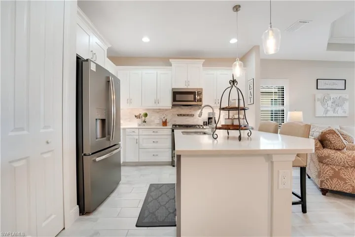 Kitchen featuring a breakfast bar area, stainless steel appliances, white cabinetry, light countertops, and pendant lighting