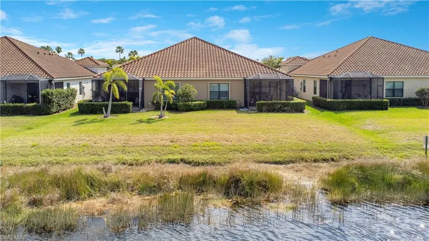 Rear view of property featuring a lanai, a water view, a lawn, and a tiled roof