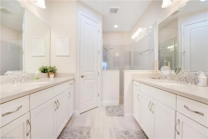 Bathroom featuring two vanities, visible vents, walk in shower, and a sink