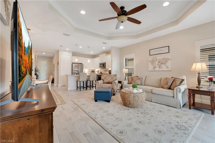 Living area featuring light wood-style flooring, recessed lighting, visible vents, ornamental molding, and a raised ceiling