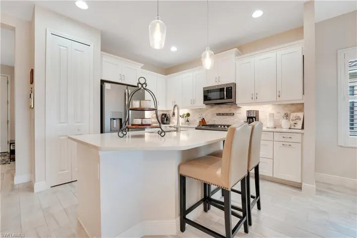 Kitchen with a kitchen island with sink, appliances with stainless steel finishes, white cabinets, and light countertops