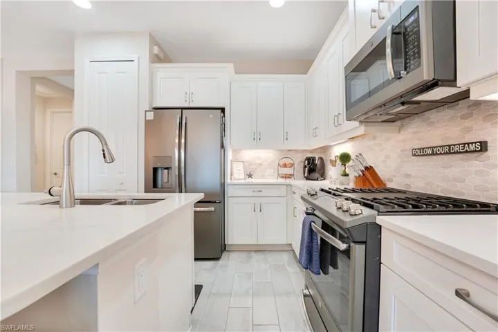 Kitchen with light stone counters, backsplash, appliances with stainless steel finishes, white cabinets, and a sink