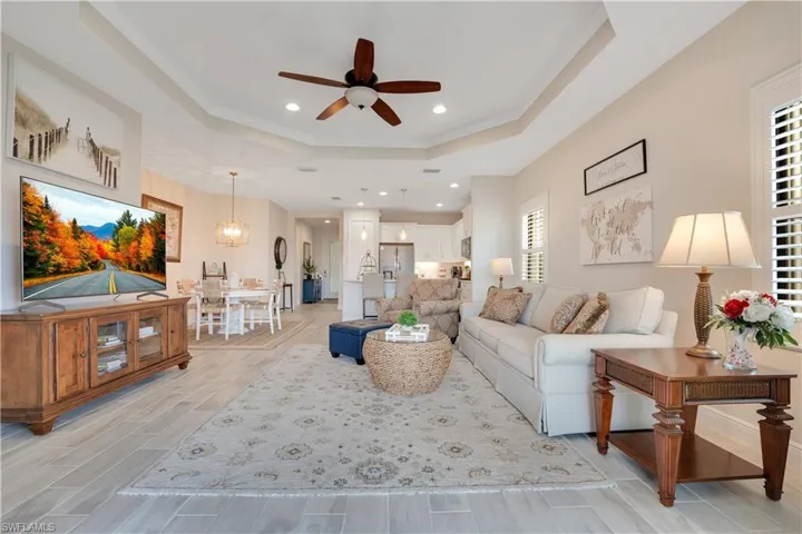 Living room with light wood-style flooring, recessed lighting, ceiling fan with notable chandelier, a raised ceiling, and crown molding