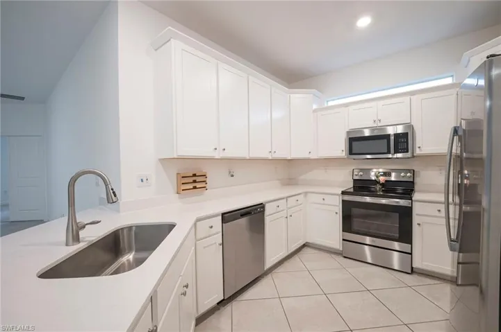 Kitchen featuring stainless steel appliances, white cabinets, light tile patterned floors, and light stone countertops