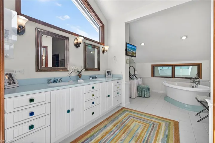 Full bath featuring plenty of natural light, double vanity, a wainscoted wall, a soaking tub, and vaulted ceiling