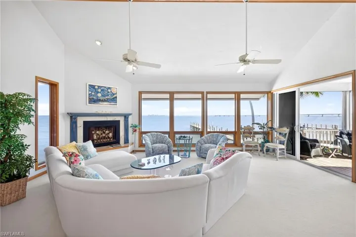Carpeted living room with a water view, high vaulted ceiling, plenty of natural light, a high end fireplace, and ceiling fan
