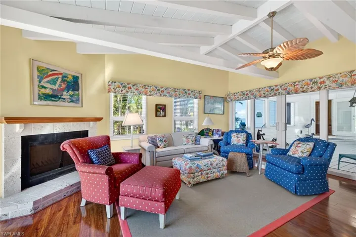 Living area with wood finished floors, a tiled fireplace, a wood ceiling with exposed beams, a ceiling fan, and high vaulted ceiling