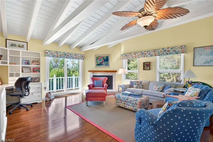 Living room with dark wood-type flooring, an office area, a fireplace with raised hearth, a ceiling fan, and wood ceiling