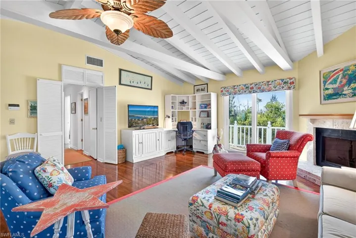 Living room with a desk, wood finished floors, a fireplace with raised hearth, wooden ceiling, and a ceiling fan
