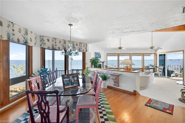 Dining space with a water view, lofted ceiling, a chandelier, wood finished floors, and a ceiling fan