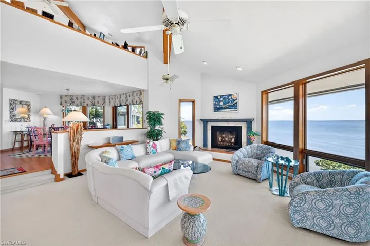 Carpeted living area featuring a fireplace with raised hearth, ceiling fan, a water view, high vaulted ceiling, and recessed lighting