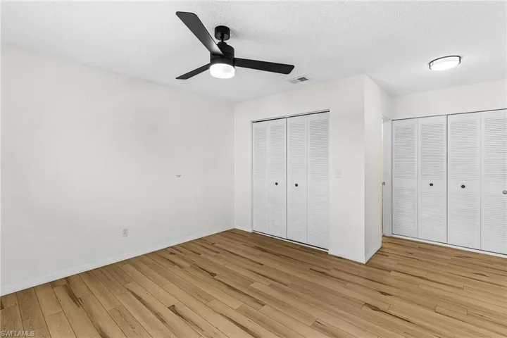 Unfurnished bedroom with multiple closets, light wood-style flooring, a textured ceiling, and ceiling fan