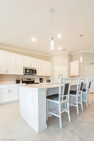Kitchen featuring stainless steel appliances, crown molding, light tile patterned floors, white cabinets, and hanging light fixtures