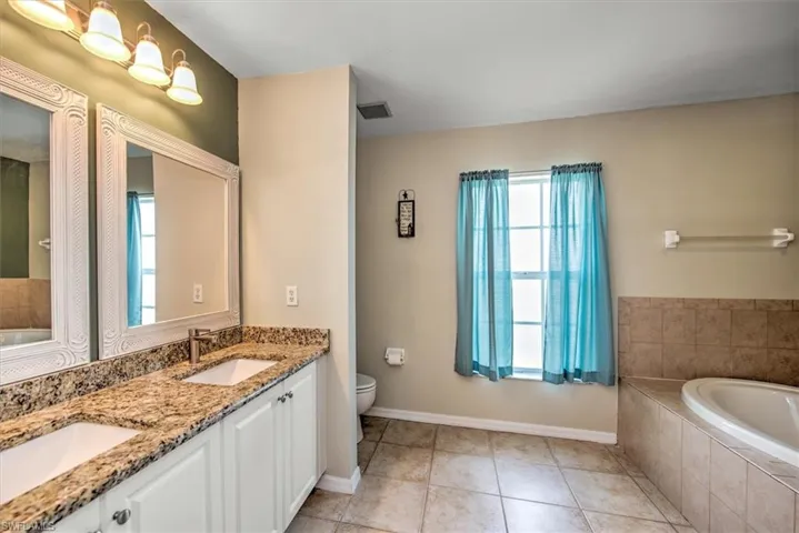 Bathroom featuring a relaxing tiled soaking tub, dual sinks, oversized vanity, tile floors, and separate shower.